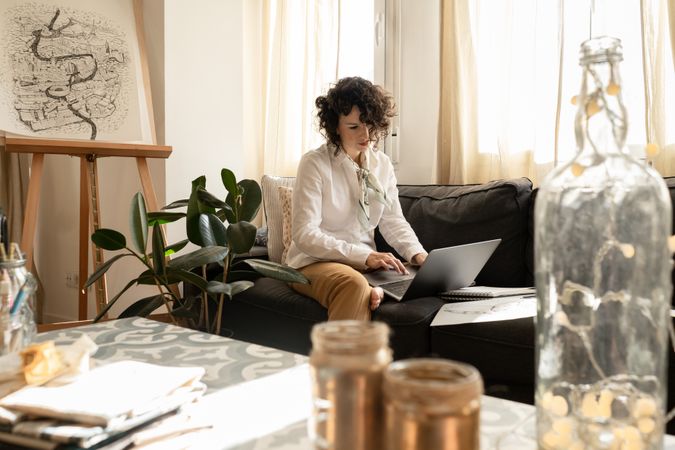 Woman using laptop near draws on papers on sofa in room