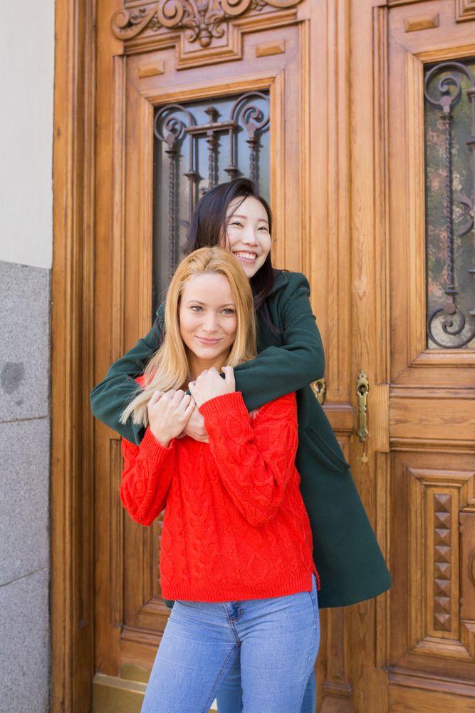 Cheerful female friends hugging near ornamental door