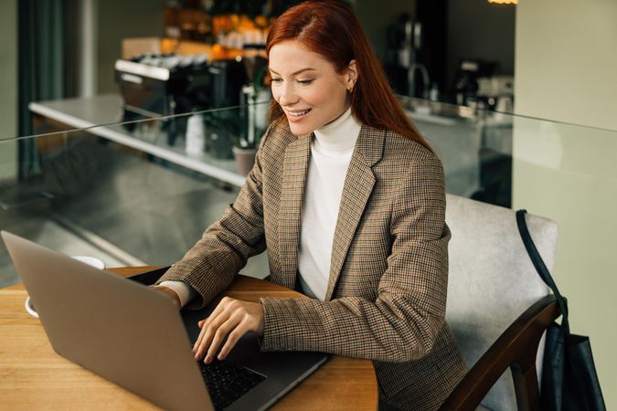 Happy woman in blazer working on laptop in cafe