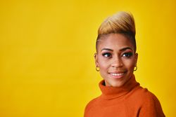 Studio shot of confident smiling Black woman posing with short blonde hair in orange sweater