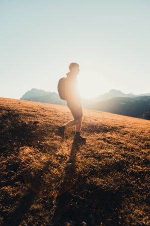 Side view of man with backpack hiking in Dolomites, Italy at sunset