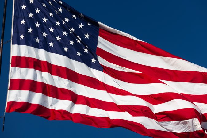 American Flag Waving In The Wind Against Deep Blue Sky.