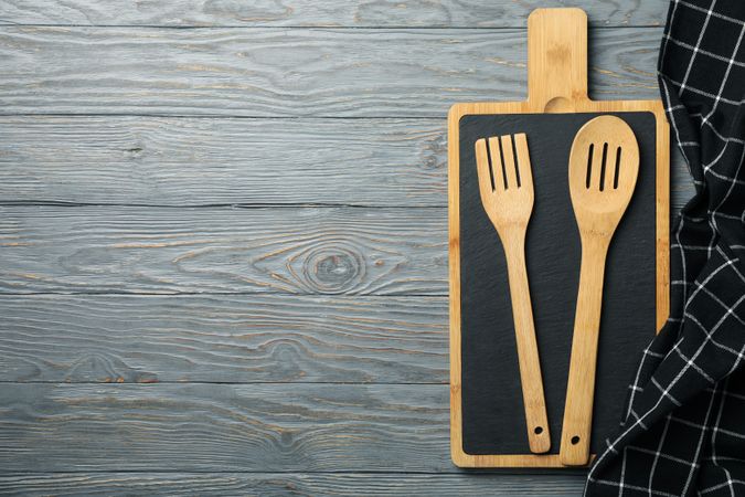 Composition with kitchen cutlery and cutting board on gray wooden background, space for text