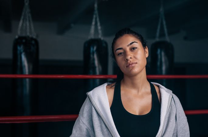 Portrait of confident female boxer standing in the ring in hoodie