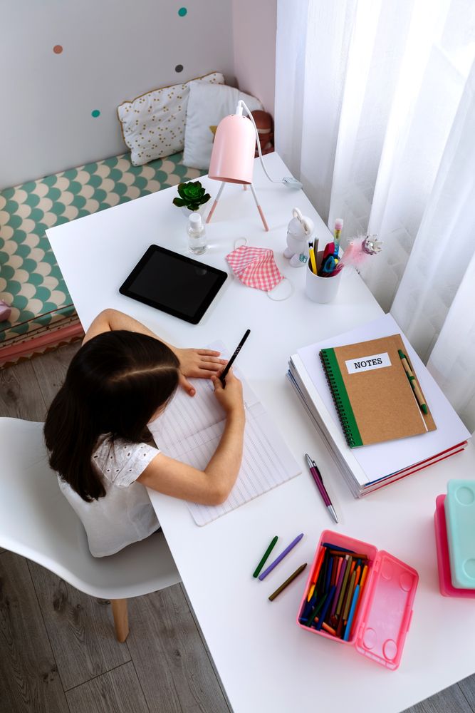 Girl studying at home with tablet and mask on table