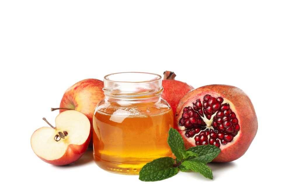 Pot of honey with dipper, open pomegranate and apples