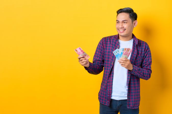 Happy young Asian man in plaid shirt holding banknotes
