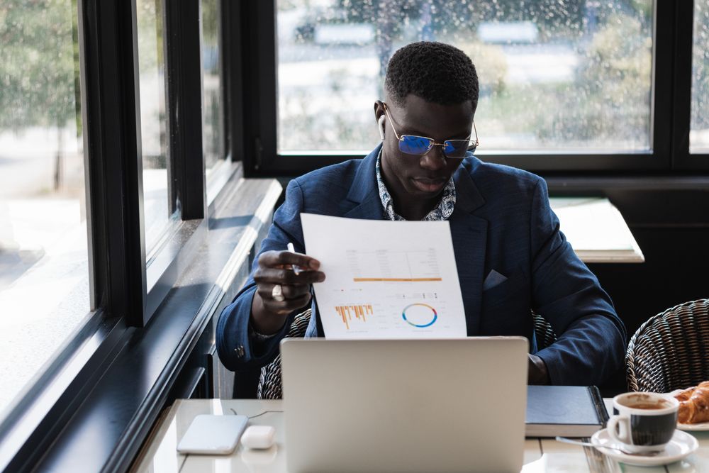 Serious Black businessman in earbud with diagram on paper indoors