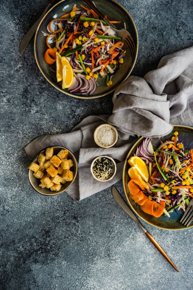 Top view of two fresh salad with finely chopped vegetables and lemon slices in bowl on table with copy space