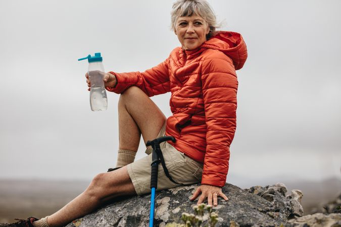 Mature woman sitting on a rock and drinking water