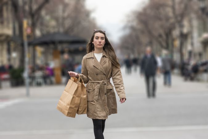 Portrait of young woman walking in a city street, with takeaway coffee in hands