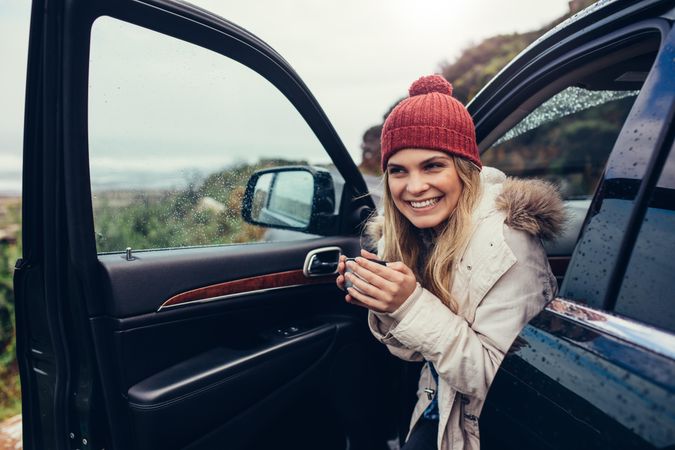Joyful woman enjoying hot coffee in her car with door open