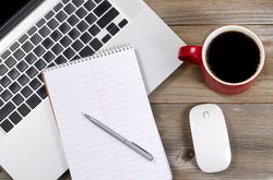 Blank notebook and pen with laptop on office desk