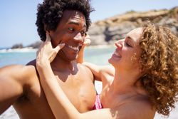 Man and woman taking silly selfie with sea in the background