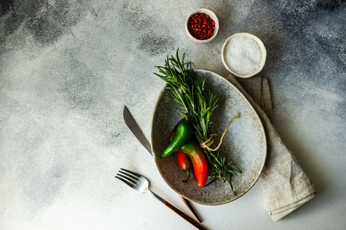 Top view of grey bowl with rosemary bunch and spicy peppers