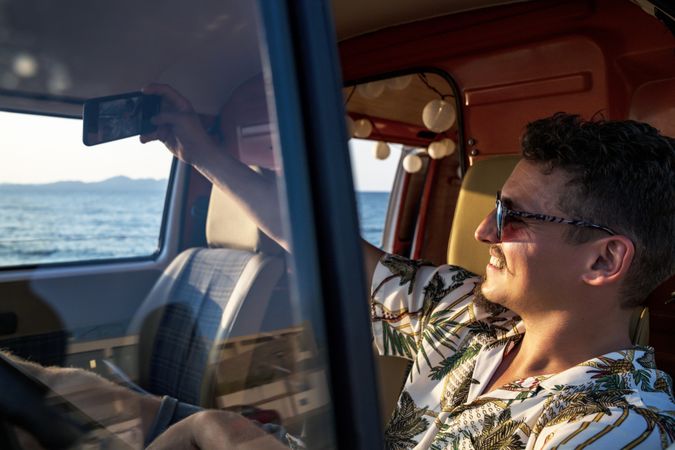 Happy adult man taking selfie with smartphone while sitting in van