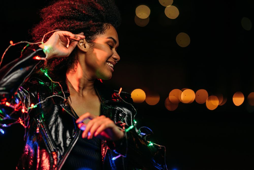 Smiling Black woman at night wrapped in holiday lights