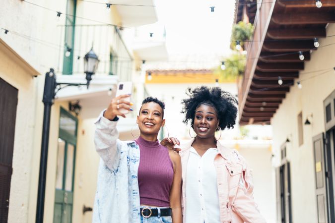 Happy women taking selfies with smartphone walking in the city
