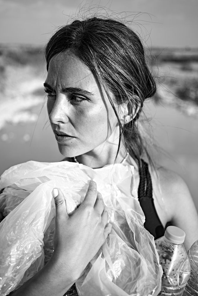 Concerned female in swimsuit collecting trash in natural lake