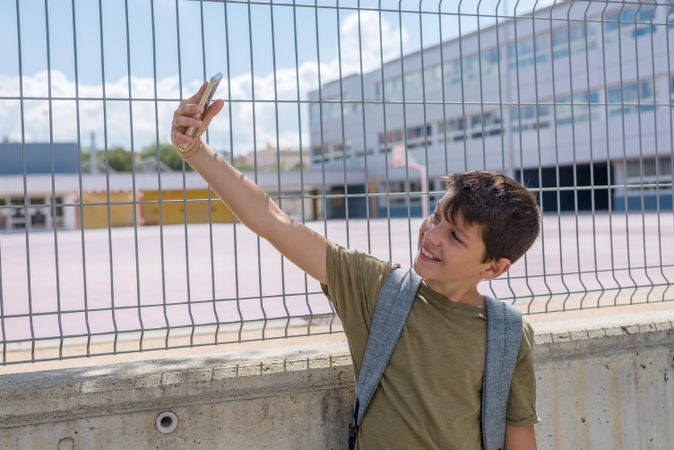 Smiling boy taking selfie on smartphone outside of school yard
