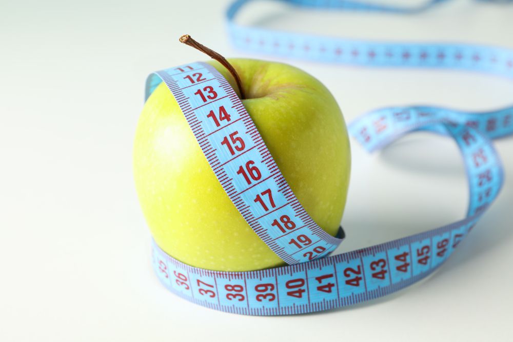 Apple with measuring tape on blank background, close up