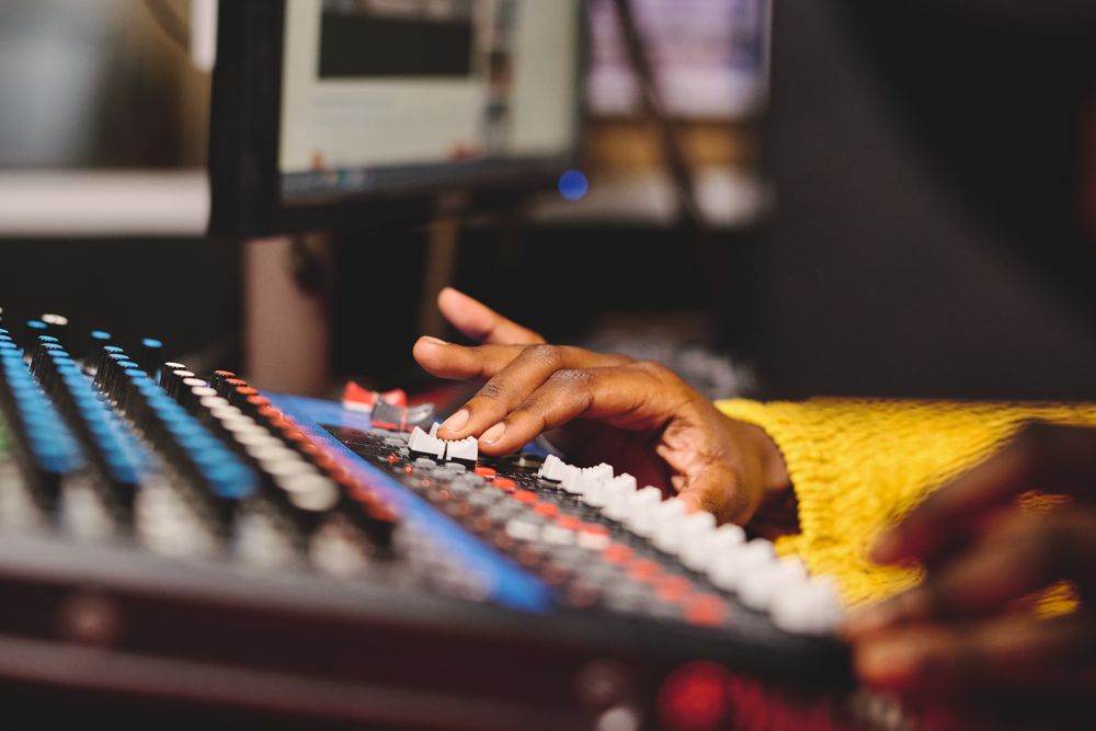 Crop Black female radio host using mixing console in studio