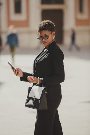 Stylish Black woman with handbag and smartphone on street