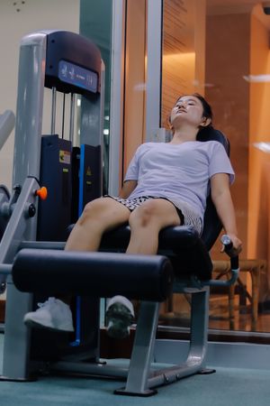 woman using leg extension machine at gym sitting with legs positioned under padded machine bar