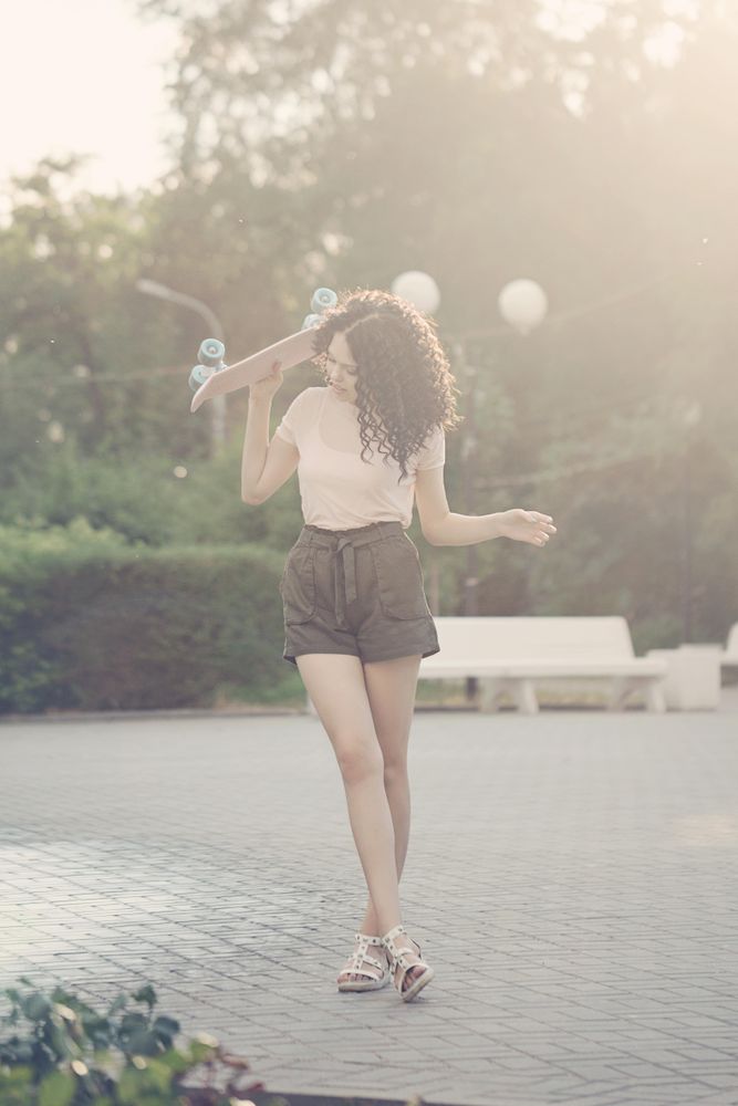 Teenager with pink skateboard behind her head at sunset