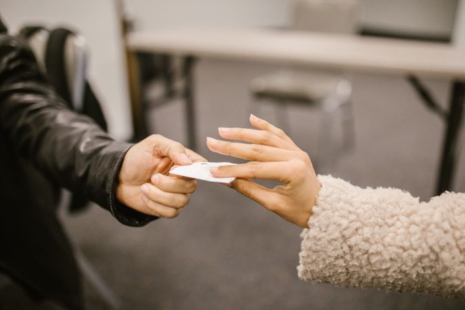 Cropped image of two students exchanging a piece of paper in classroom