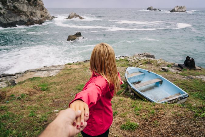 Woman holding hand of crop person inviting to follow to seashore with boat