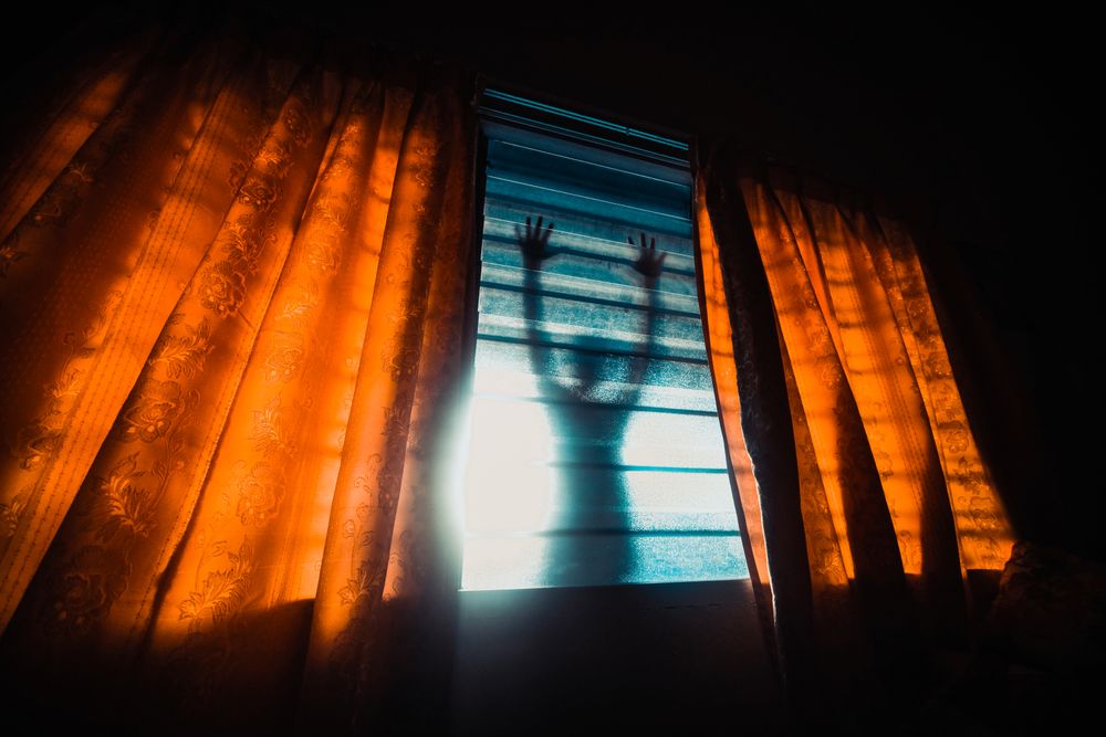 Shadow of person leaning on a window in a dark room