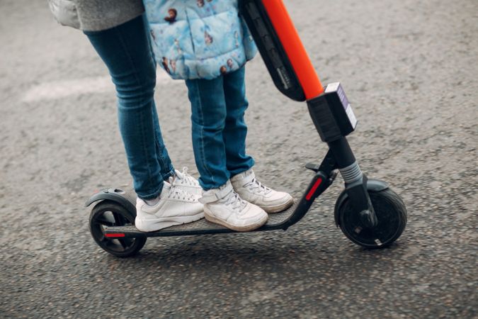 Cropped image of two children riding a red kick scooter