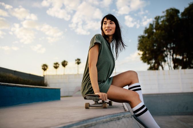 Woman sitting on skateboard relaxing at skate park with palm trees