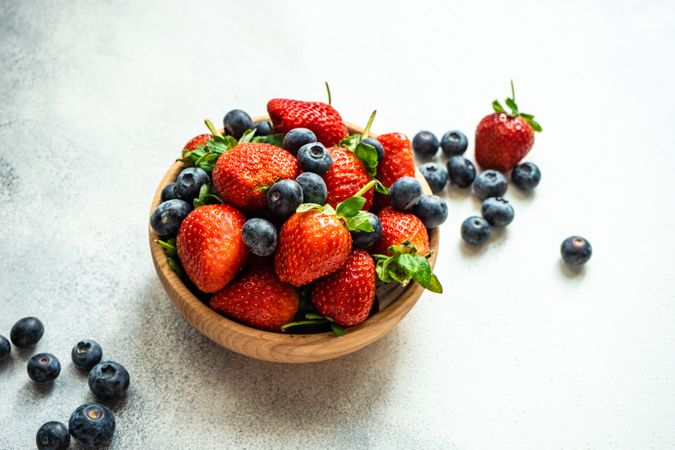 Summer berries in wooden bowl full on stone background with copy space