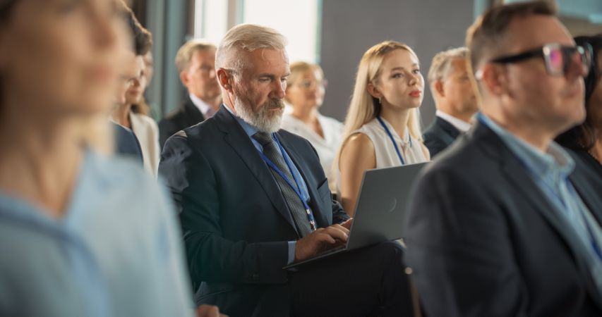 Male Top Manager Sitting In Crowd And Using Laptop Computer At International Technology Conference.