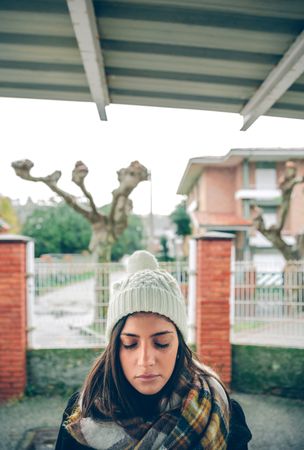 Woman in warm clothes standing outside with eyes closed in front of face