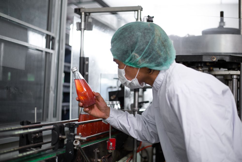Asian man worker inspecting drink product on bottling factory machinery.