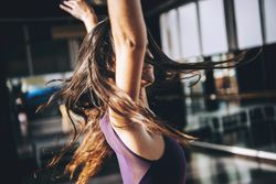 Young brunette with long waving hair moving while dancing in sunlight.
