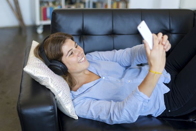 Young smiling woman lying on a sofa taking selfie on her phone