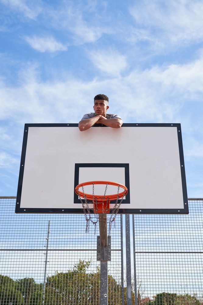 Male climbing on basketball backboard in outdoor sports ground
