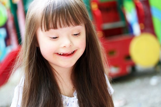 Portrait of a young girl with Down syndrome looking down in a playground