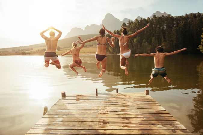 Portrait of young friends jumping from jetty into lake