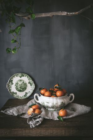 Orange tangerines in ceramic ornamental bowl on wooden table