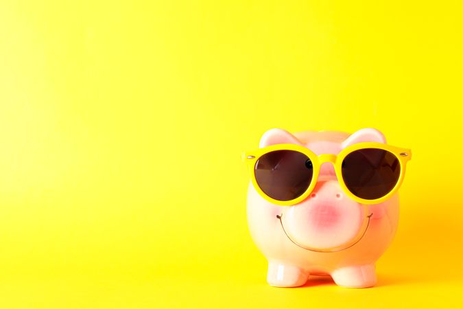 Happy piggy bank with sunglasses on yellow background, space for text. Finance, saving money