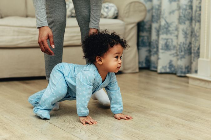 Baby boy crawling on the floor with mother standing over him