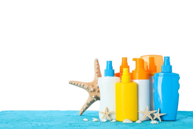 Different sunscreen sprays with starfishes and seashells on color table isolated on studio background. Safe tan