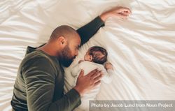 Top view of newborn baby boy sleeping with his father on bed 56gWl4