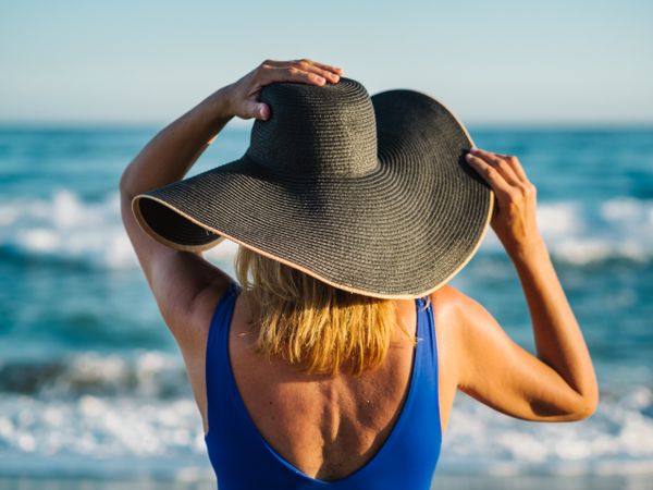 Woman in blue swimsuit and hat on sandy beach