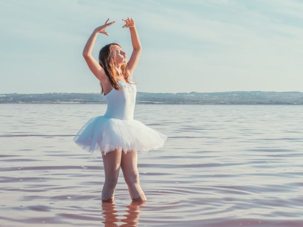 Ballerina in swimsuit with tutu performing classical position in water